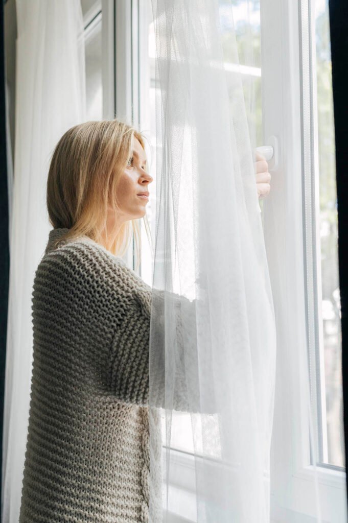 _side-view-sad-woman-home-pandemic-looking-through-window