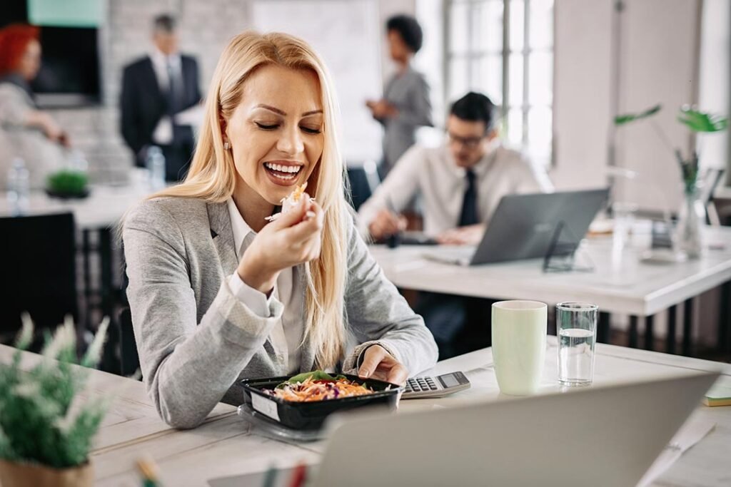_mujer-de-negocios-sonriente-comiendo-alimentos-saludables-en-el-trabajo-y-comiendo-ensalada-de-verduras-para-el-almuerzo